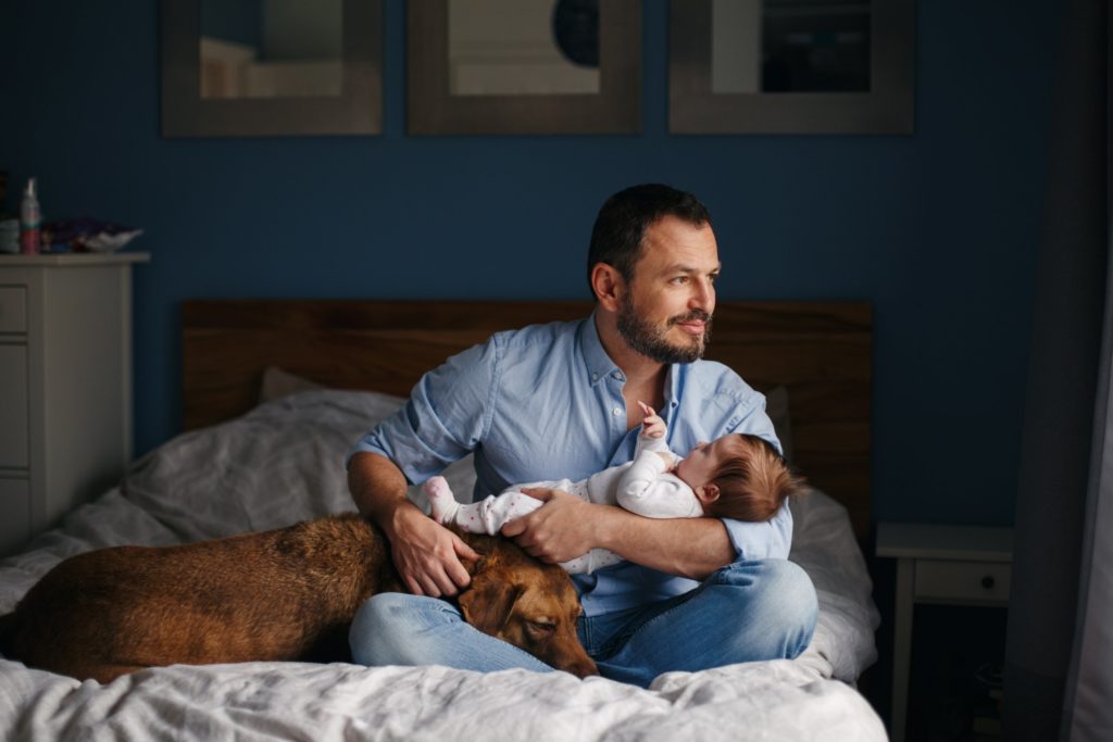 A man holds his dog and his new baby.